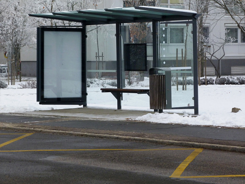empty modern glass bus shelter in wintry setting with snow and billboard poster sign case for advertisement with bare trees in the background