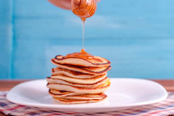 istock Pouring honey onto tasty thin folded pancakes on plate against white background 1084967824