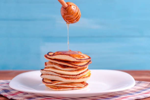 istock Pouring honey onto tasty thin folded pancakes on plate against white background 1084967834