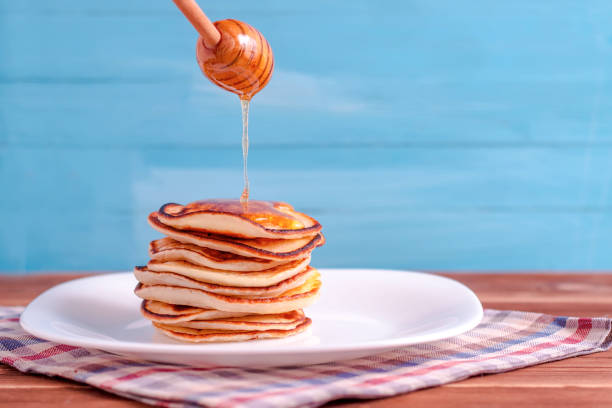 istock Pouring honey onto tasty thin folded pancakes on plate against white background 1084967844