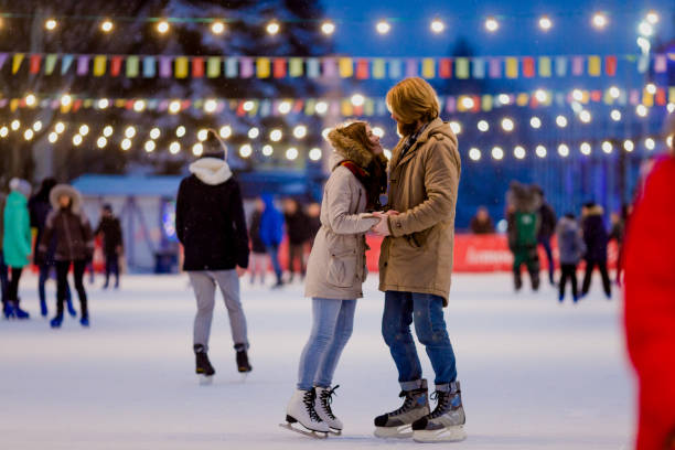 Young couple in love Caucasian man with blond hair with long hair and beard and beautiful woman have fun, active date skating on ice scene in town square in winter on Christmas Eve Young couple in love Caucasian man with blond hair with long hair and beard and beautiful woman have fun, active date ice skating on the ice arena in the evening city square in winter on Christmas Eve ice skating stock pictures, royalty-free photos & images