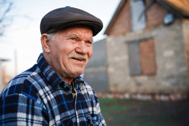 Happy smiling elder senior man portrait with a mustache in a cap on the background of a brick house in a Russian village Happy smiling elder senior man portrait with a mustache in a cap on the background of a brick house in a Russian village russian ethnicity stock pictures, royalty-free photos & images