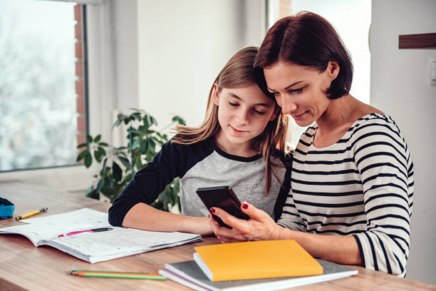 madre che usa lo smartphone e aiuta la figlia con i compiti - child telephone mobile phone little girls foto e immagini stock