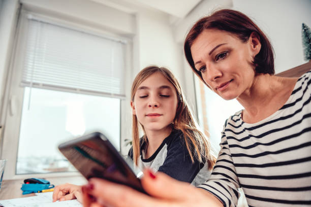 istock Mother using smart phone and helping daughter with homework 1084982352