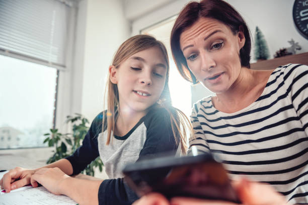 istock Mother using smart phone and helping daughter with homework 1084982462