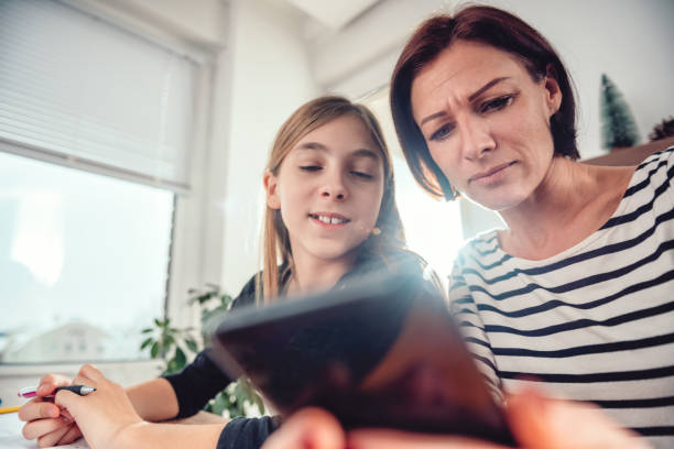 istock Mother using smart phone and helping daughter with homework 1084982636