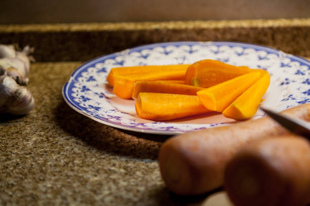Pieces of chopped carrots lie on a plate. Next on the marble table is garlic and a whole carrot