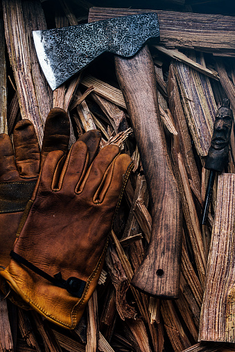 Old axe and yellow leather glove with a piled pieces of firewood