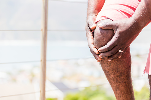 A male african person having severe knee pain.