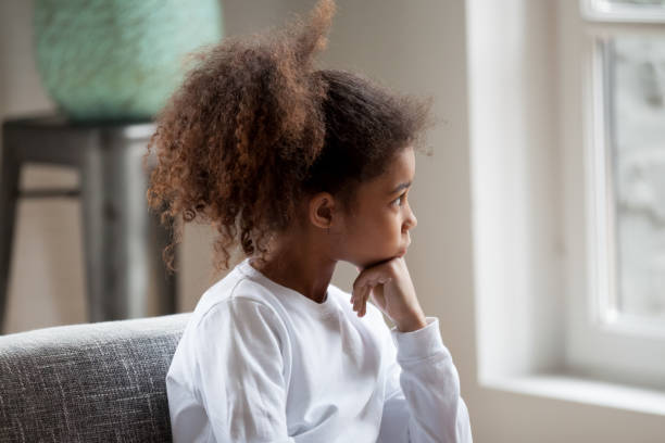 thoughtful african american ragazza prescolare che guarda alla finestra - child sadness little girls thinking foto e immagini stock