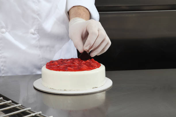 istock hands pastry chef prepares a cake, cover with icing and decorate with strawberries, works on a stainless steel industrial kitchen work top 1085011902