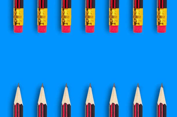 istock Two rows of new wooden graphite pencils with rubber eraser tip scattered on blue background with copy space for your text 1085014654