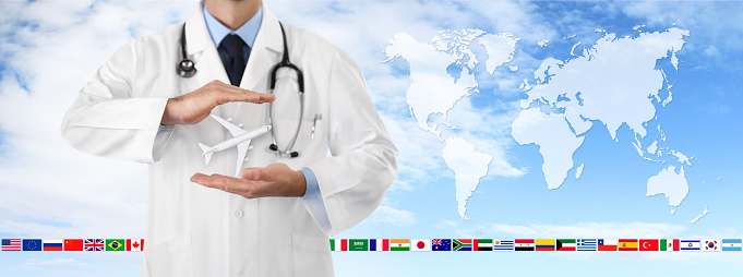 travel medical insurance concept, doctor's hands protect an airplane on blue sky background with flags and world map