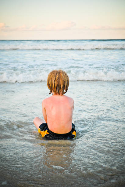 young boy sitting in the waves stock photo