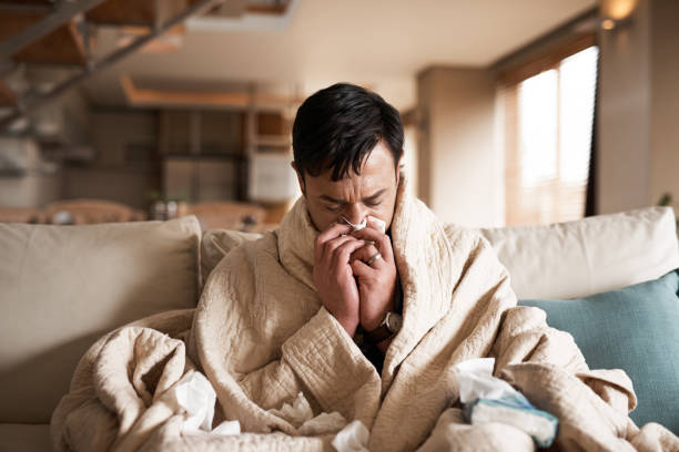 It's the season of sneezes Cropped shot of a young man suffering with flu while sitting wrapped in a blanket on the sofa at home cold and flu man stock pictures, royalty-free photos & images