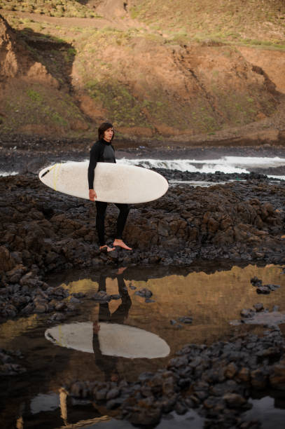 istock Brunette guy standing with a surf in his hands on the rock beach 1085022258