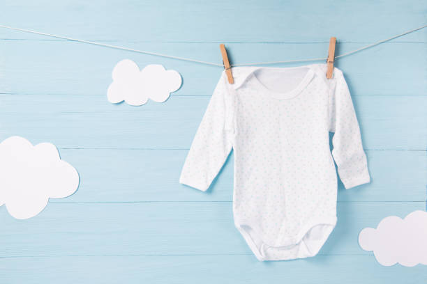 Baby clothes and white clouds on a clothesline, blue background Baby clothes and white clouds on a clothesline, blue wooden background baby clothing stock pictures, royalty-free photos & images