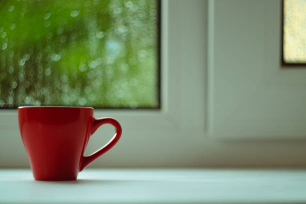 istock The red espresso cup on white windowsill. On background window and rain. Cup located at left of frame. 1085051952