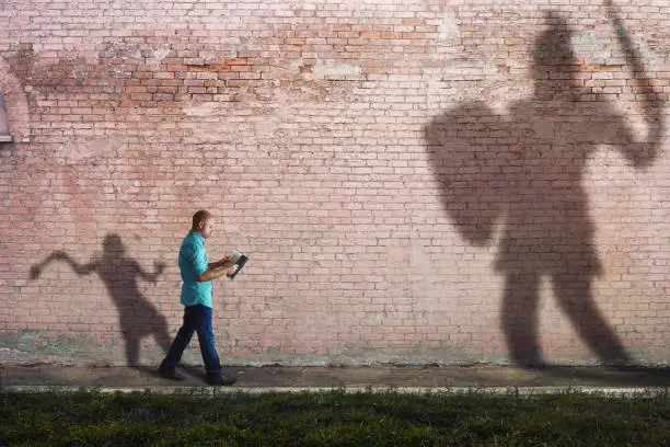 A man reads a Bible while his shadow is David fighting goliath.