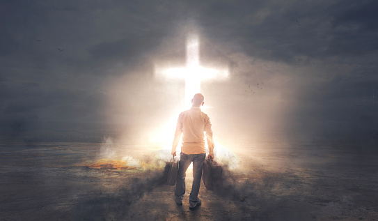 A man carrying baggages of darkness before a bright glowing cross