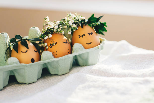 istock Happy Easter,  rustic eco concept. Stylish easter eggs in floral wreaths and  cute faces in carton tray. Modern cute easter eggs with flowers crown and sleepy eyes in sunny light. Space for text 1085055066