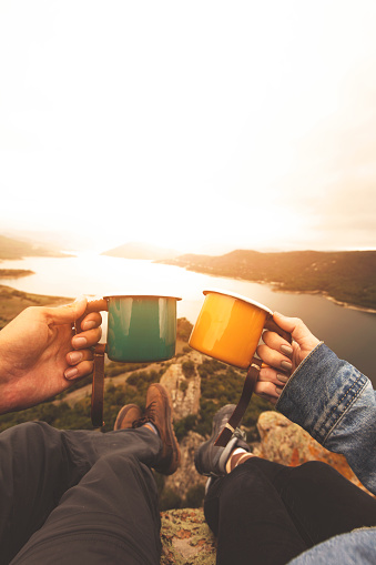 Pov image of couple holding enamel cups on mountain peak