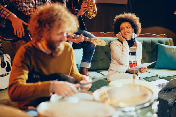 Caucasian talented drummer playing drums. Caucasian talented drummer playing drums. In background mixed race woman having earphones on ears and smiling. Home studio interior. drumstick stock pictures, royalty-free photos & images