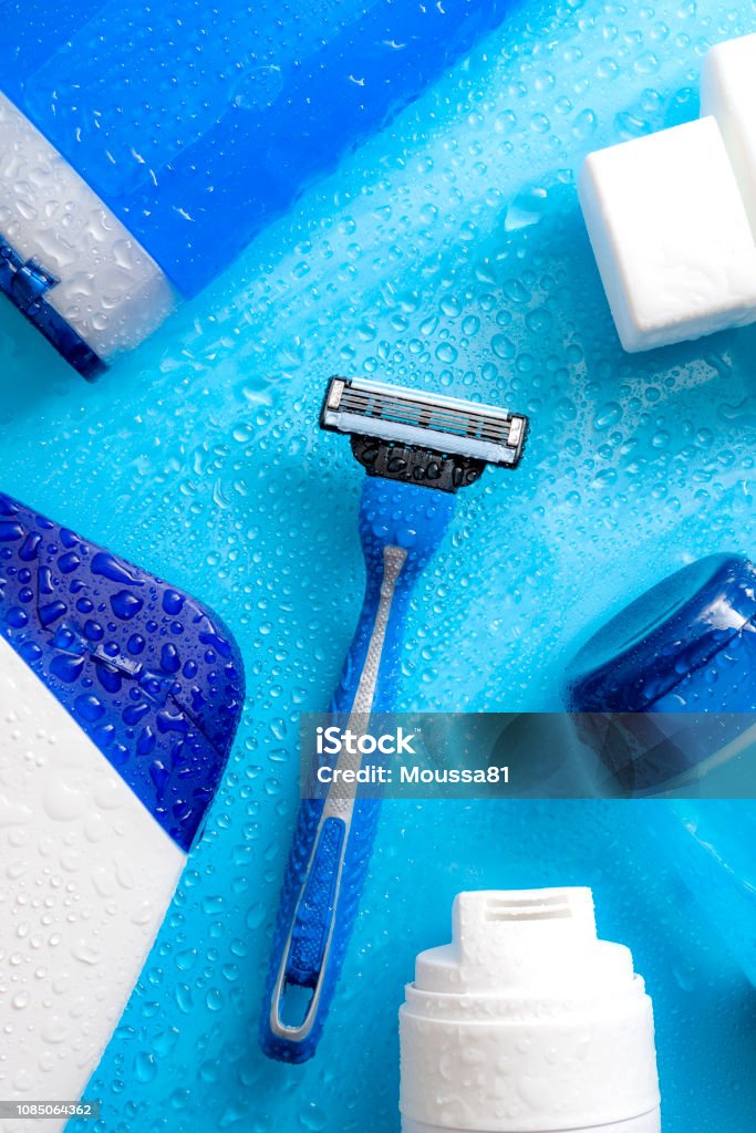 Men cosmetic products, personal hygiene and male hair care and shaving concept with kit of masculine shampoo, aftershave, body wash, gel and razor soaked in water droplets on wet light blue background Razor Stock Photo