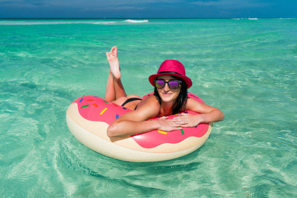 sorridente bella donna bruna con cappello rosa nuota su un grande tubo gonfiabile sulla costa del mar dei caraibi - swimming tube inflatable circle foto e immagini stock