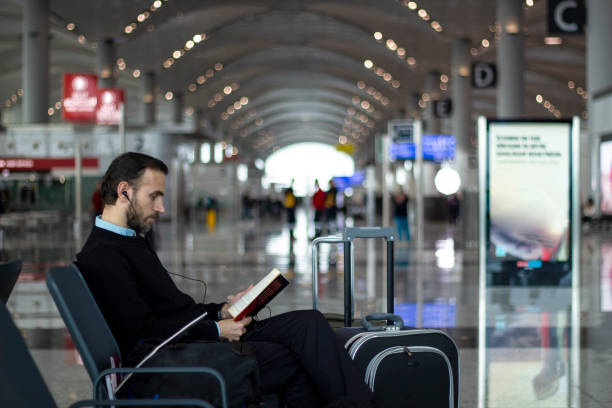 lecture d’un livre tout en écoutant de la musique à la salle d’embarquement à l’aéroport de passagers - salle dembarquement photos et images de collection