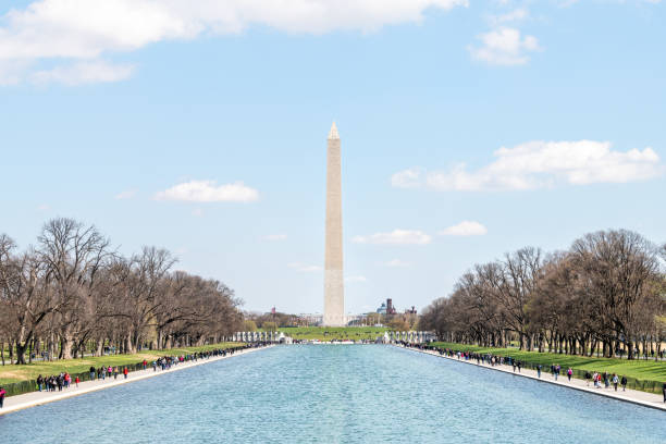 Washington Monument in center, tourists, people walking by Lincoln Memorial and reflecting pool on national mall during green spring sunny day, blue water Washington DC, USA - April 5, 2018: Washington Monument in center, tourists, people walking by Lincoln Memorial and reflecting pool on national mall during green spring sunny day, blue water washington monument reflecting pool stock pictures, royalty-free photos & images