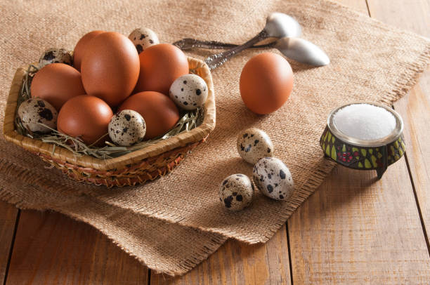 istock Large brown chicken eggs and small mottled quail eggs, two teaspoons and salt on wooden table. 1085077412