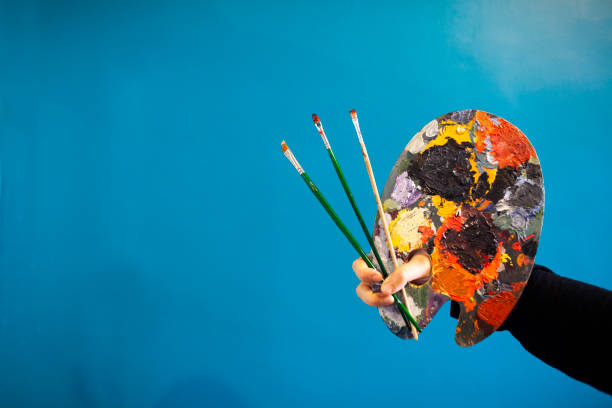 istock woman holding paint brush and pallette on blue background 1085081236