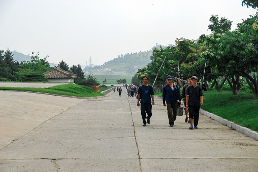 Nampo, North Korea - 27 July 2014. Workers returning from work walking across a paved road on a collective farm