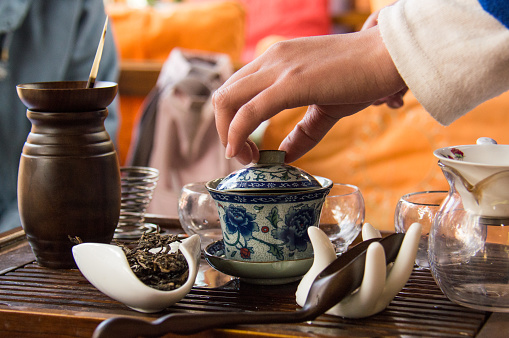 A tea ceremony with Puer tea in Lijiang, China. A female hand lifts the lid from a blue and white teapot.