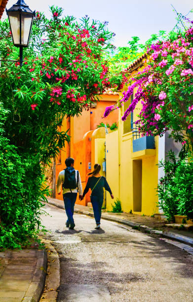 Exploring PlaKa Athens, Greece-May 2, 2018-A young couple hold hands as they stroll the narrow lanes past colorful residential facades and under a profusion of blooming shrubs. plaka athens stock pictures, royalty-free photos & images