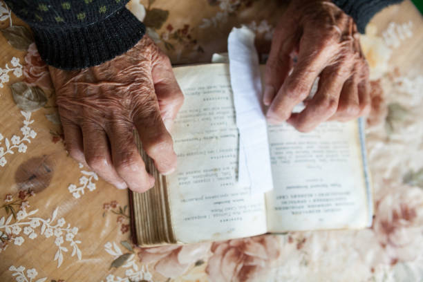 istock Old woman hands on the open prayer book. 1085099640