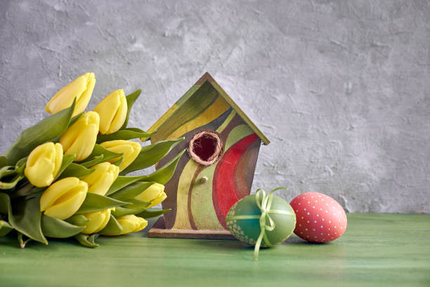 istock Easter decorations on gray concrete background. Yellow tulips, birdhouse and painted Easter eggs 1085100762