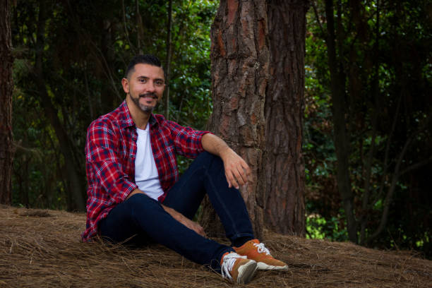 istock Handsome man on lumberjack check shirt sitting by pine tree in forest 1085104490