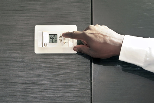 Male hand try to turn on the new air condition in room, in the hotel room. African man hands on the air conditioning control panel. Hand setting temperature air condition.