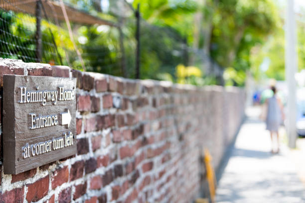 Sign for Ernest Hemingway Home, residence, museum, direction to entrance at corner turn left information on red brick wall at sidewalk street, road, people in background Key West, USA - May 1, 2018: Sign for Ernest Hemingway Home, residence, museum, direction to entrance at corner turn left information on red brick wall at sidewalk street, road, people in background hemingway house stock pictures, royalty-free photos & images