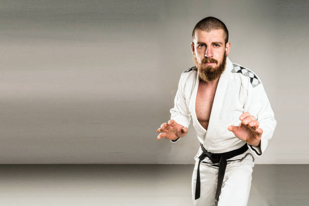 Fighter in white Kimono In A fighting Stance Judoka BJJ Jiu Jitsu Fighter in a white Kimono Gi Wearing Black Belt Standing ready for the sparing competition training session. On a plain background. Brazilian jiu jitsu brazilian jiu jitsu photos stock pictures, royalty-free photos & images