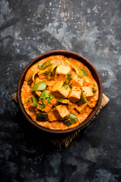 Malai or achari Paneer in a gravy made using red gravy and green capsicum. served in a bowl. selective focus stock photo