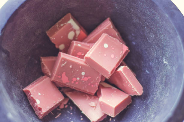 Broken and shattered pieces of ruby red chocolate in a round charcoal stone ceramic bowl. White and brwon background. Speckled chocolate.Broken and shattered pieces of ruby red chocolate in a round charcoal stone ceramic bowl. White and brown background. Speckled chocolate.