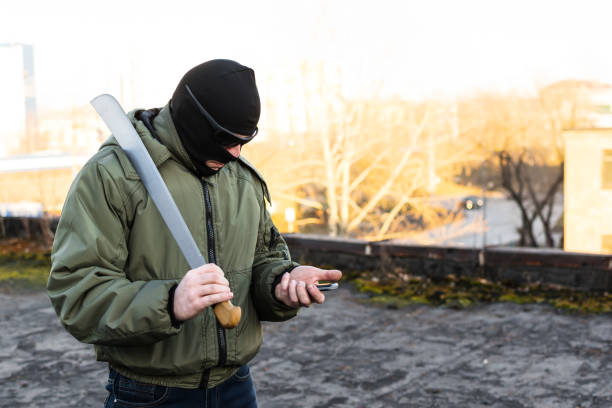 Bandit, criminal and masked man looking into the phone The bandit in a mask and a knife in his hand looks nervously into the phone Machete stock pictures, royalty-free photos & images