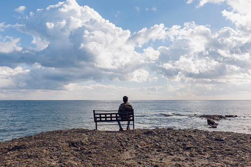 Young man on a bench, looking at the sea.
