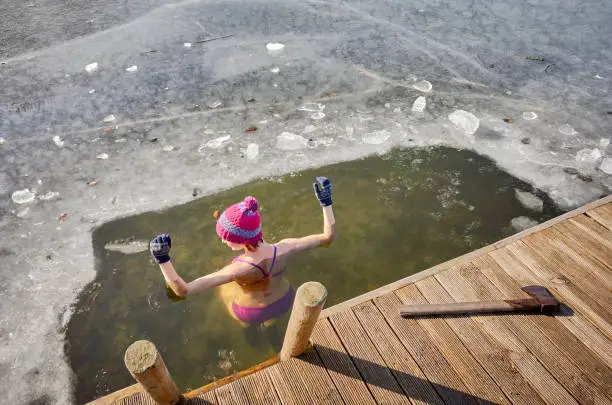 Fit woman performs ice swim in the ice hole. Holding hands above the water protects from fast hypothermia.