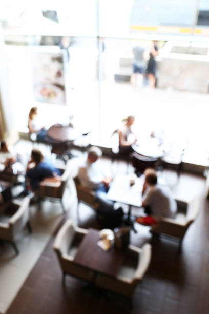 Small crowded cafe with people around the tables. It is blured background.