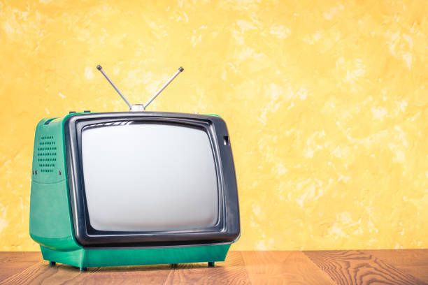 istock Retro old outdated green TV receiver from circa 70s on wooden table front textured yellow concrete wall background. Vintage style filtered photo 1085228320
