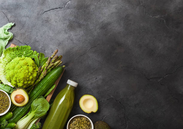 istock Assorted green toned raw organic vegetables on dark background. Avocado, cabbage, cauliflower and cucumber with trimmed beans and bottle of smoothie. 1085255370